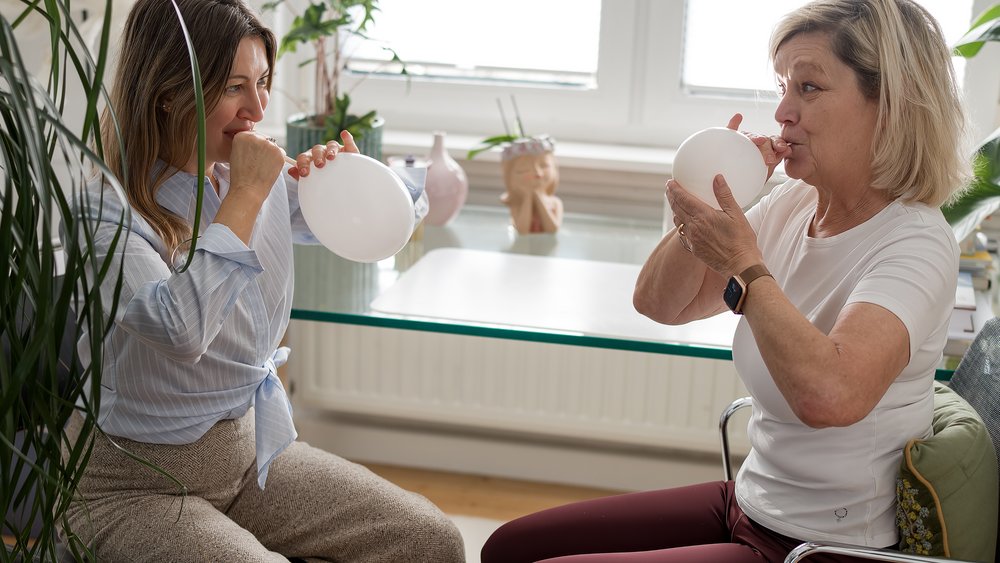Atemübungen mit Luftballons Therapeutin und Patientin üben gemeinsam eine Atemübung mit weißen Luftballons in einem freundlichen Therapieraum.