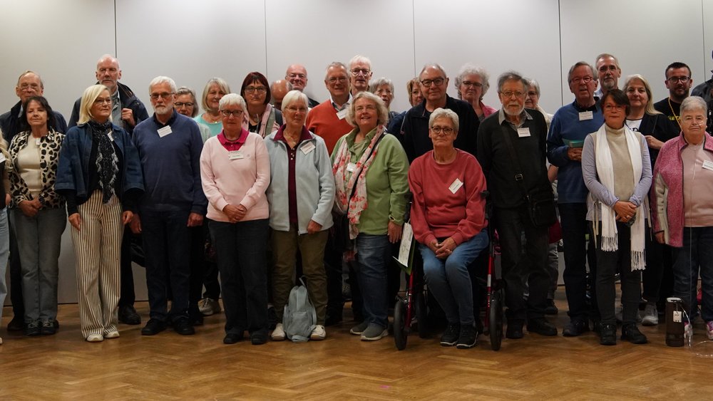 Gruppenfoto von mehr als 50 Teilnehmern des Patiententags 2024 des Lungenfibrose in Frankfurt am Main. Die Gruppe steht und sitzt in mehreren Reihen in einem hellen Veranstaltungssaal mit Parkettboden. Einige der Personen tragen Sauerstoffgeräte, zwei sitzen auf Rollatoren.